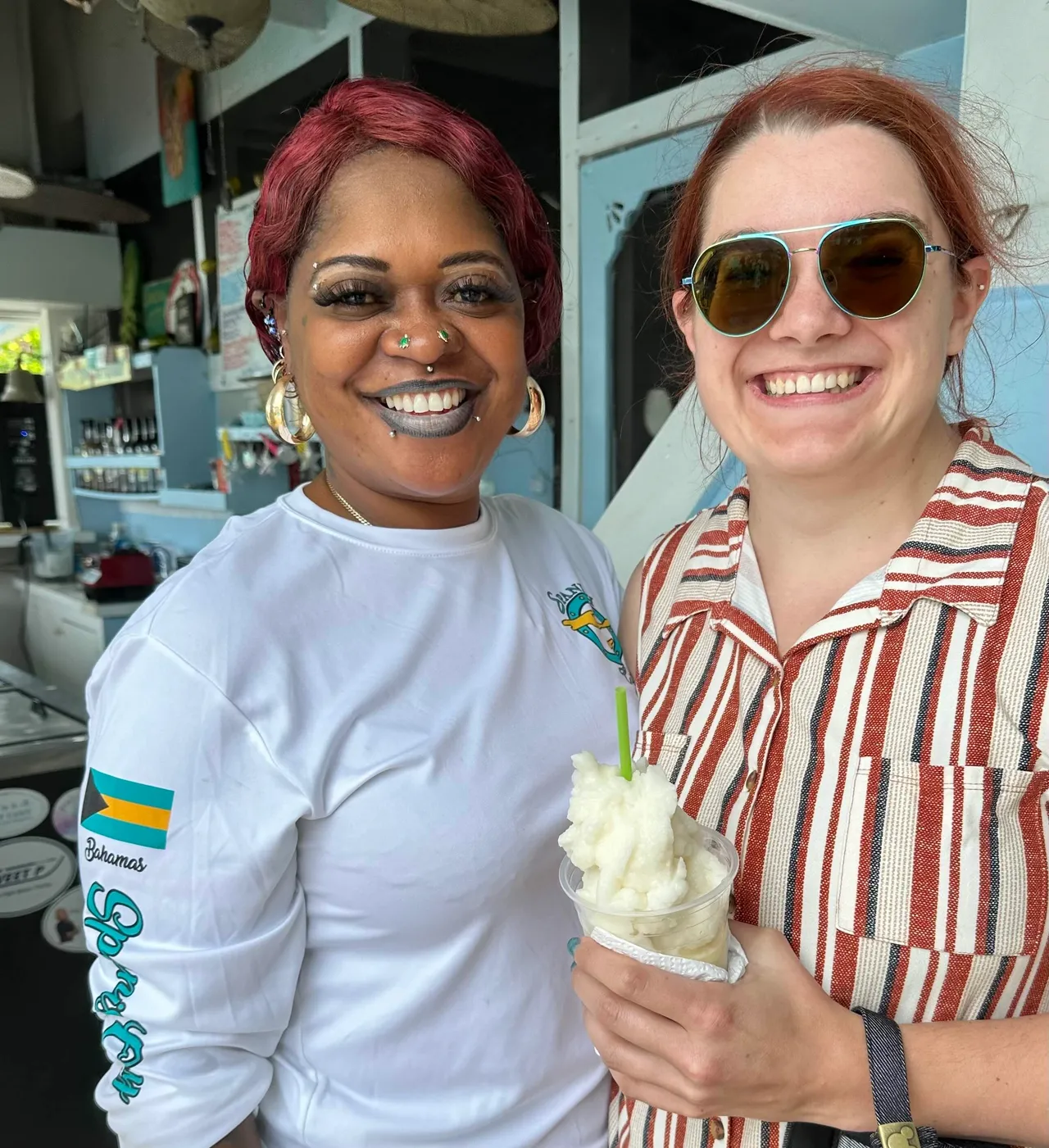 Two women holding a cold pina colada drink with smiles on.