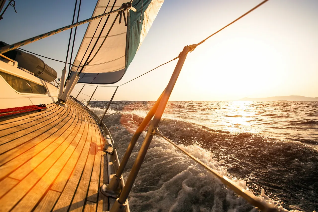View from a sailboat that is heeling over slightly under sail, with the sun in the distance.